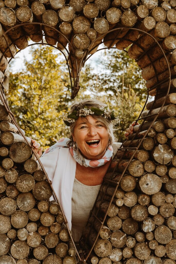 Fotografin Allgäu - Lachende Frau blickt durch ein herzförmiges Fenster in einem Holzstapel.